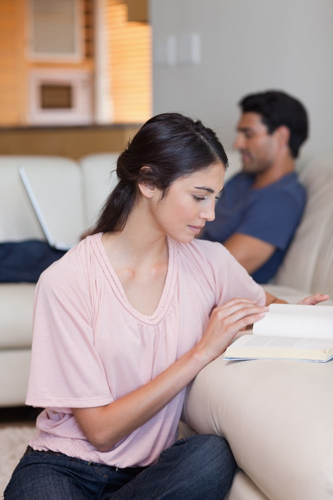 Woman reading book while husband using laptop