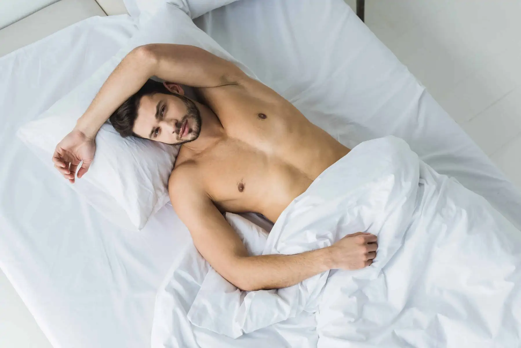 A shirtless man laying in a bed with white sheets