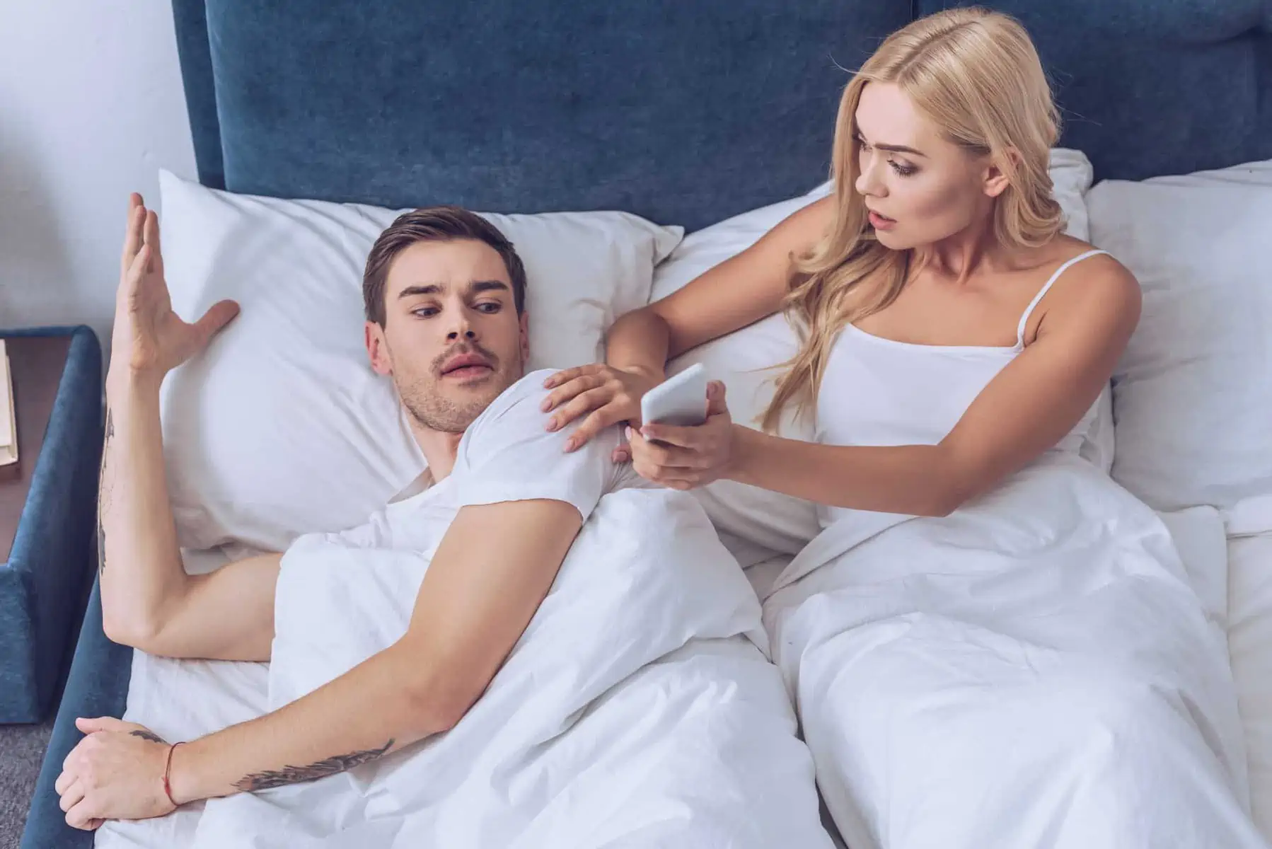 A man laying in bed next to a woman using a cell phone