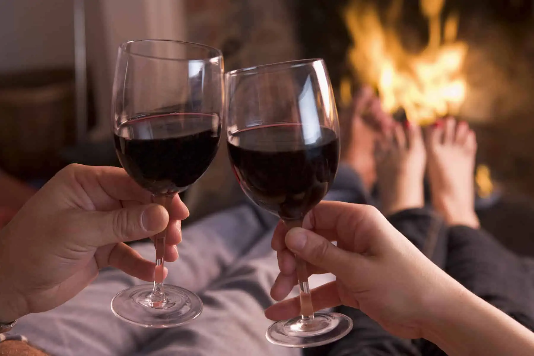 Two people toasting with red wine in front of a fireplace