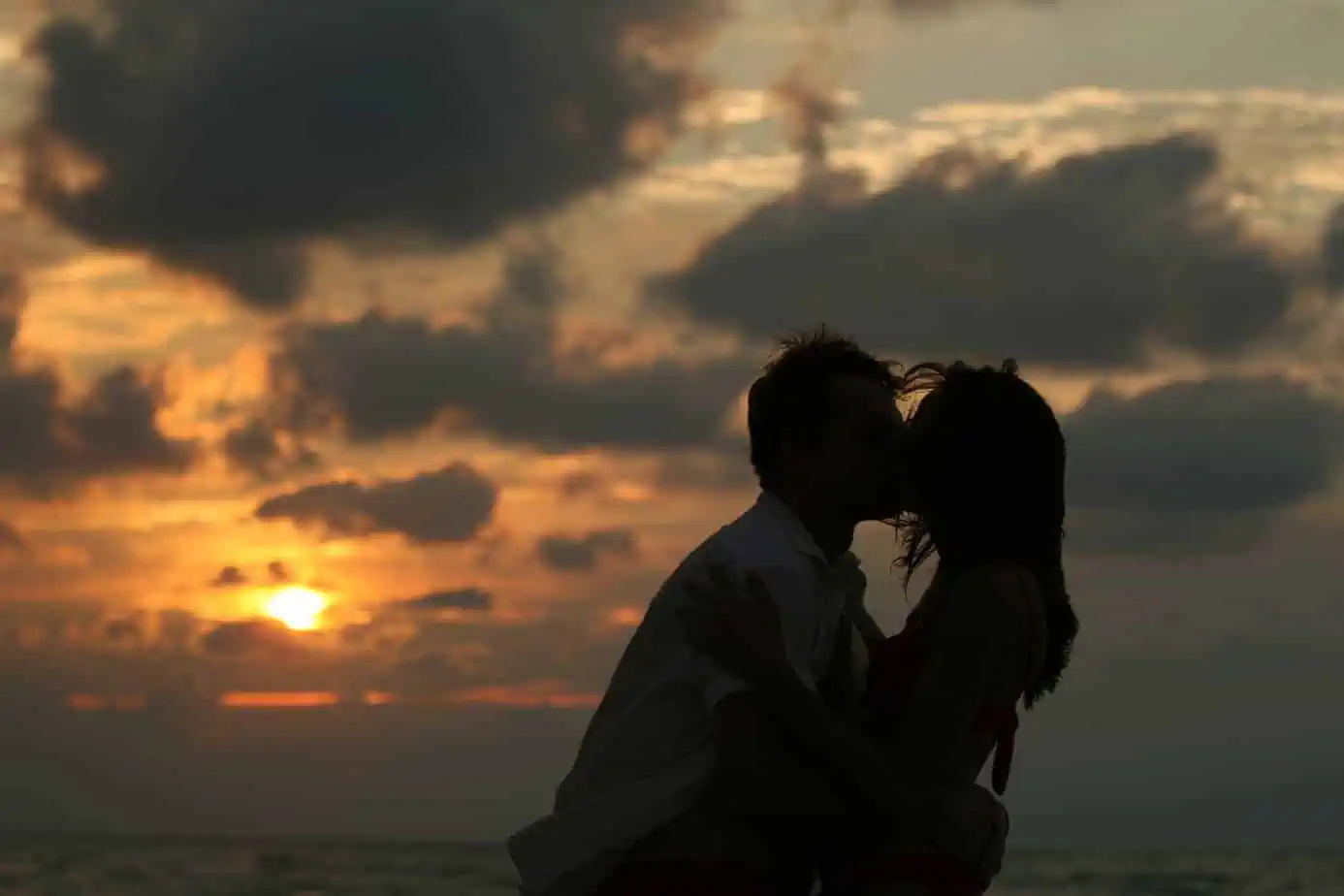A man and woman kissing on the beach at sunset