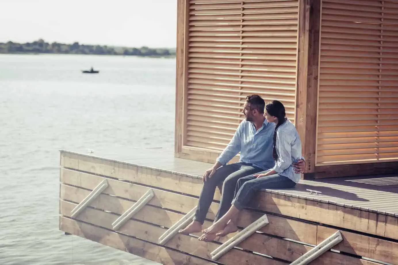 A man and a woman sitting on a dock next to a body of water