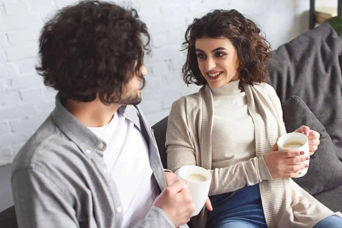 A man and a woman sitting on a couch drinking coffee