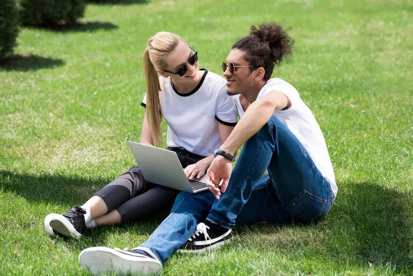 A man and woman sitting on the grass with a laptop