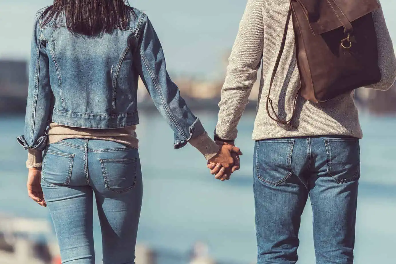 A man and a woman holding hands while walking by the water