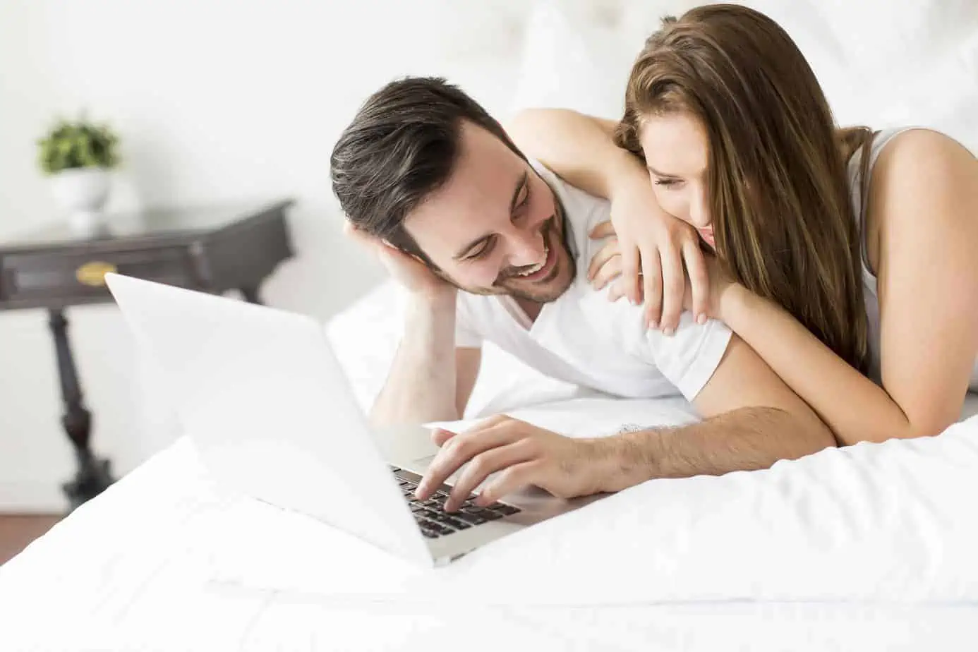 A man and woman laying in bed looking at a laptop