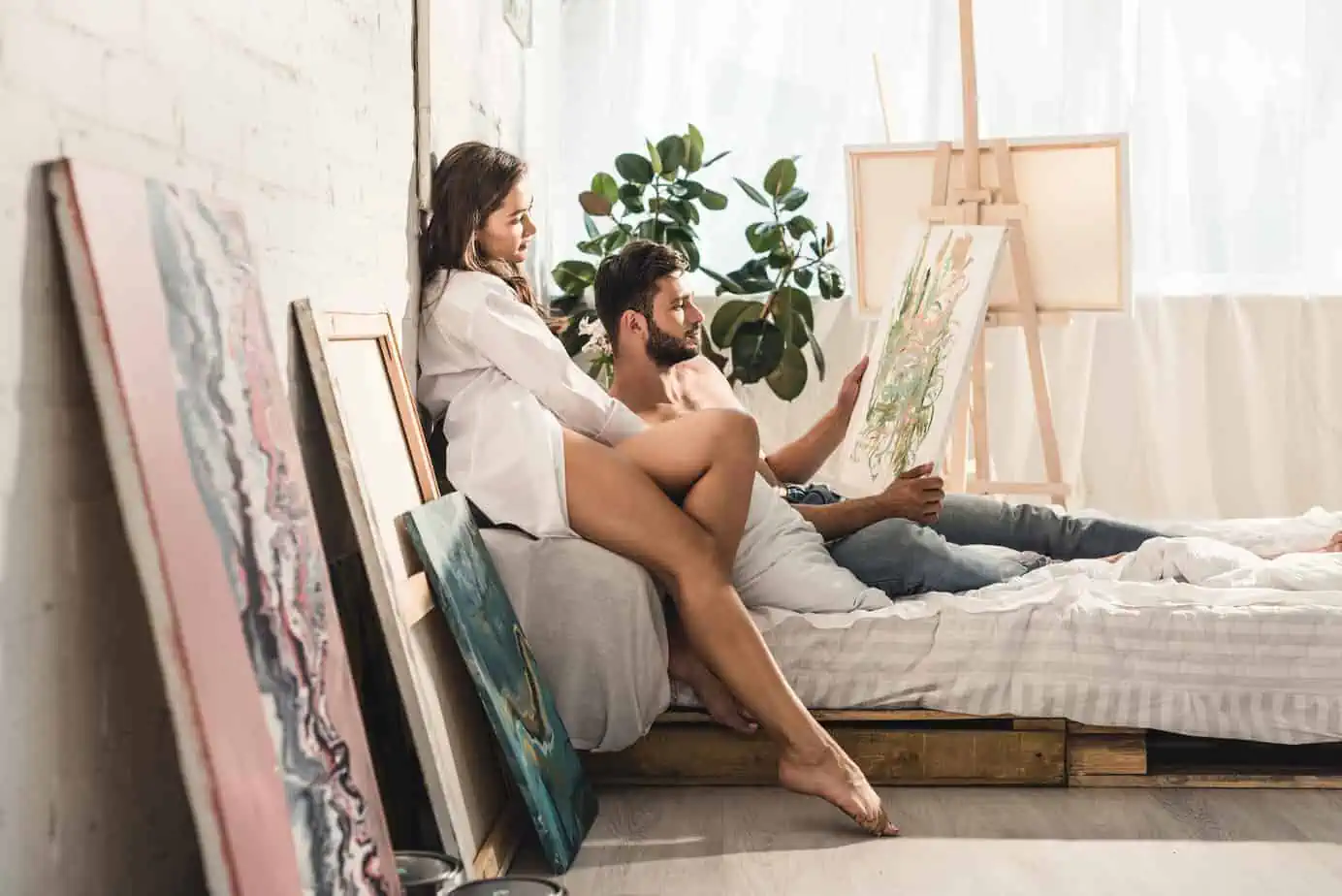 A man and woman sitting on a bed looking at a map