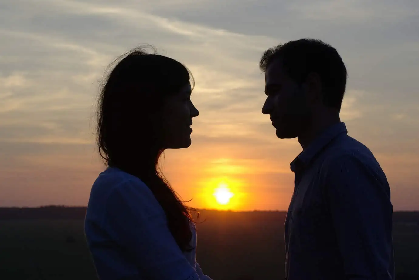 A man and a woman standing in front of a sunset