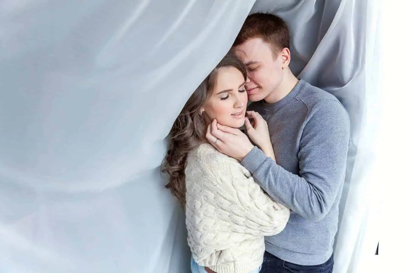 A man and a woman cuddle in front of a curtain