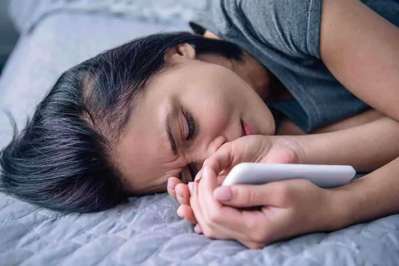 A woman sleeping on a bed holding a remote control