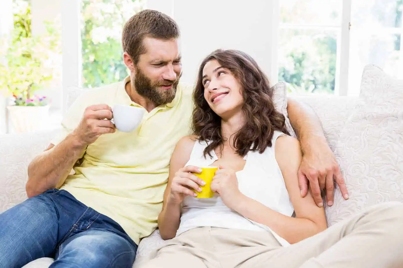 A man and woman sitting on a couch drinking coffee
