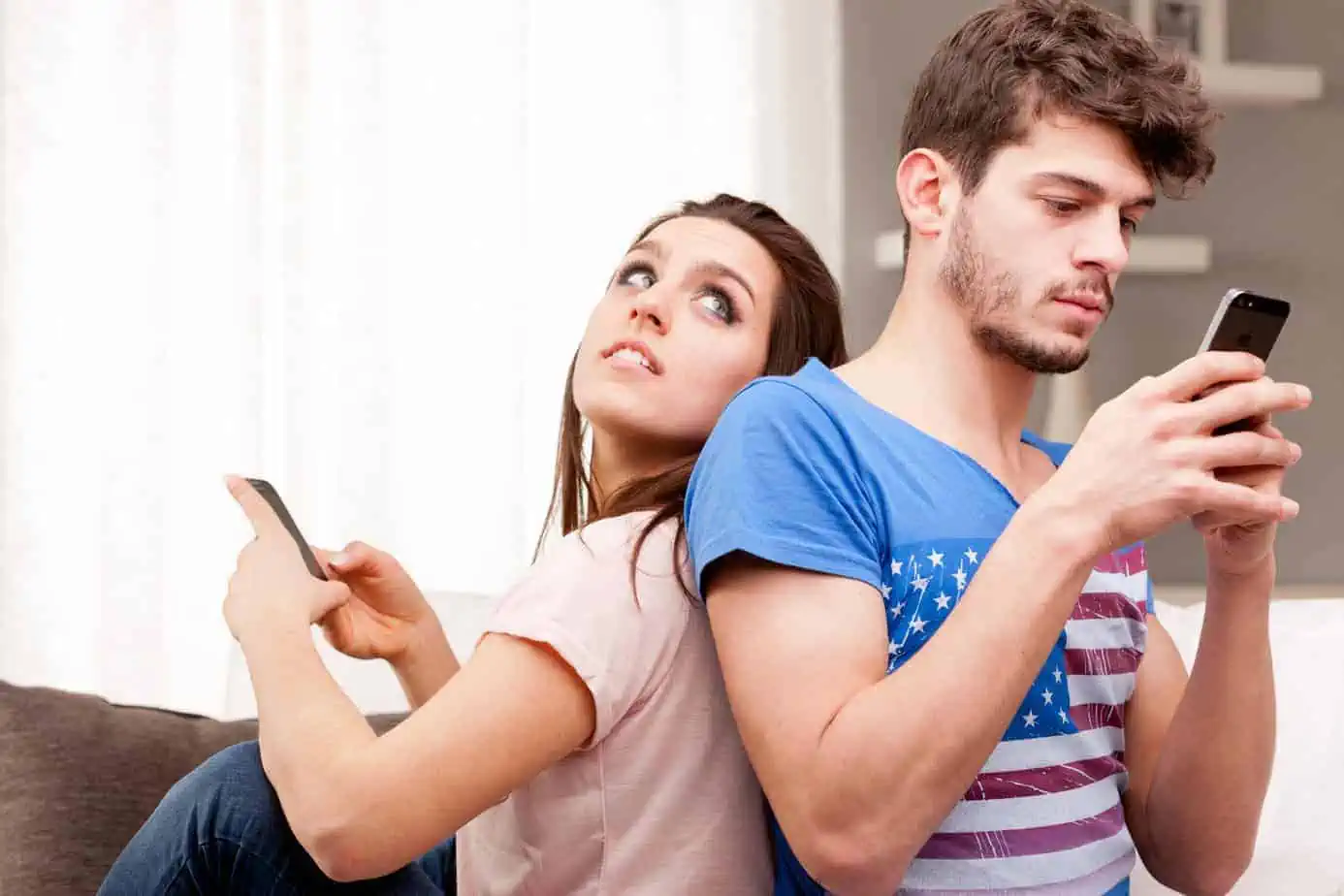 A man and woman sitting on a couch looking at a cell phone