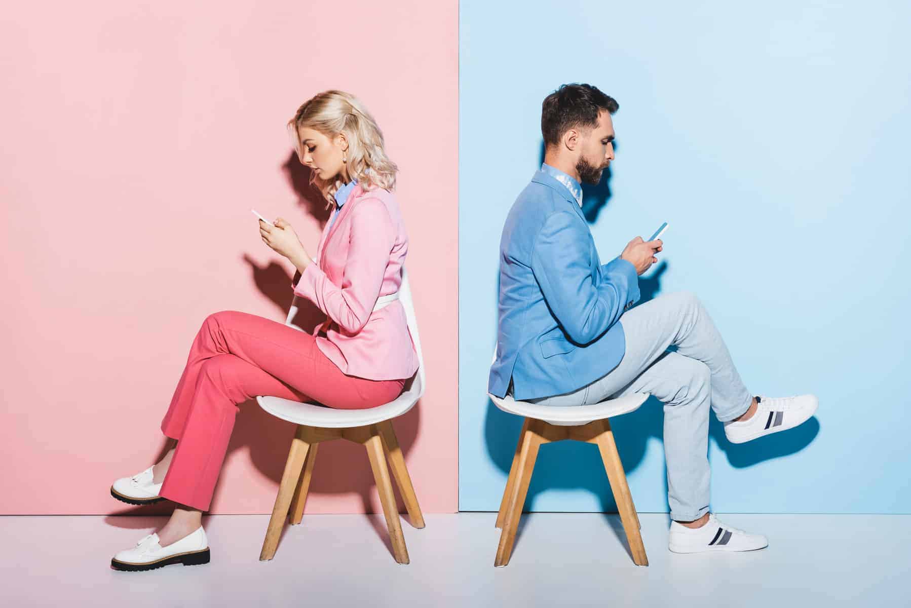 A man and a woman sitting on chairs looking at their phones