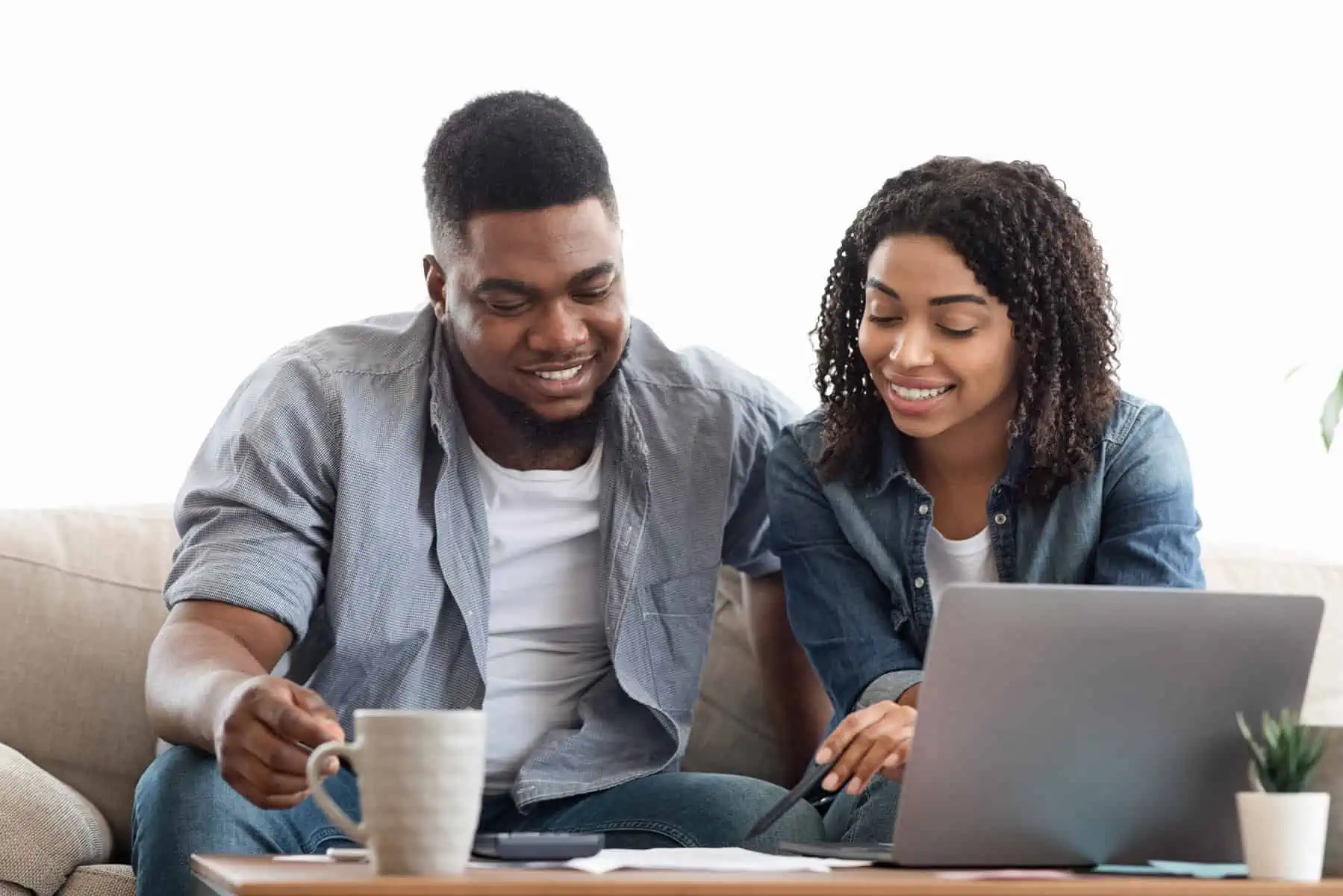 A man and woman sitting on a couch looking at a laptop