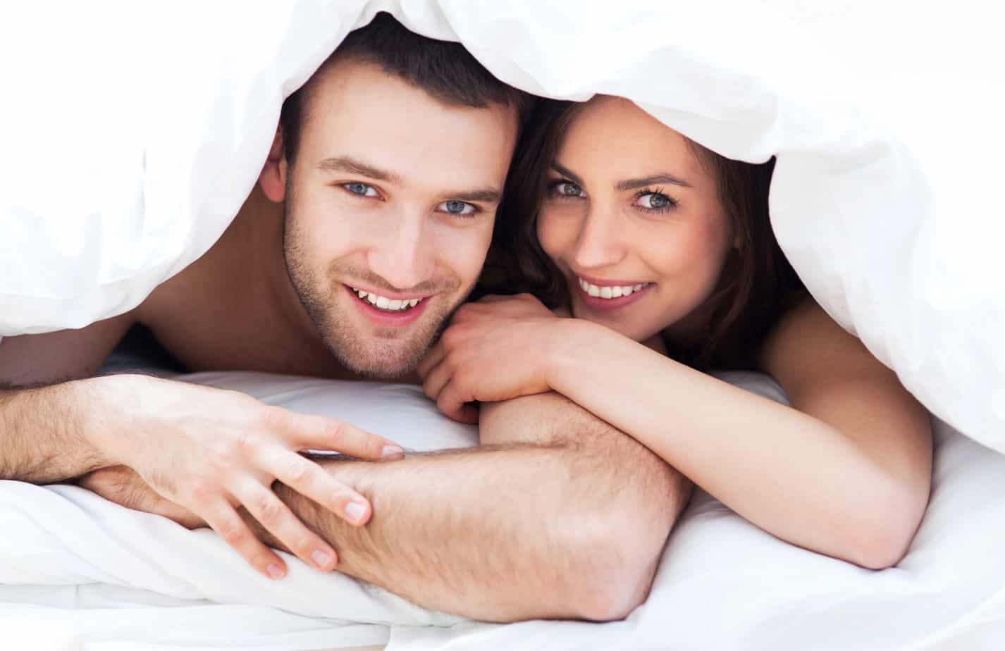 A man and woman laying in bed under a blanket