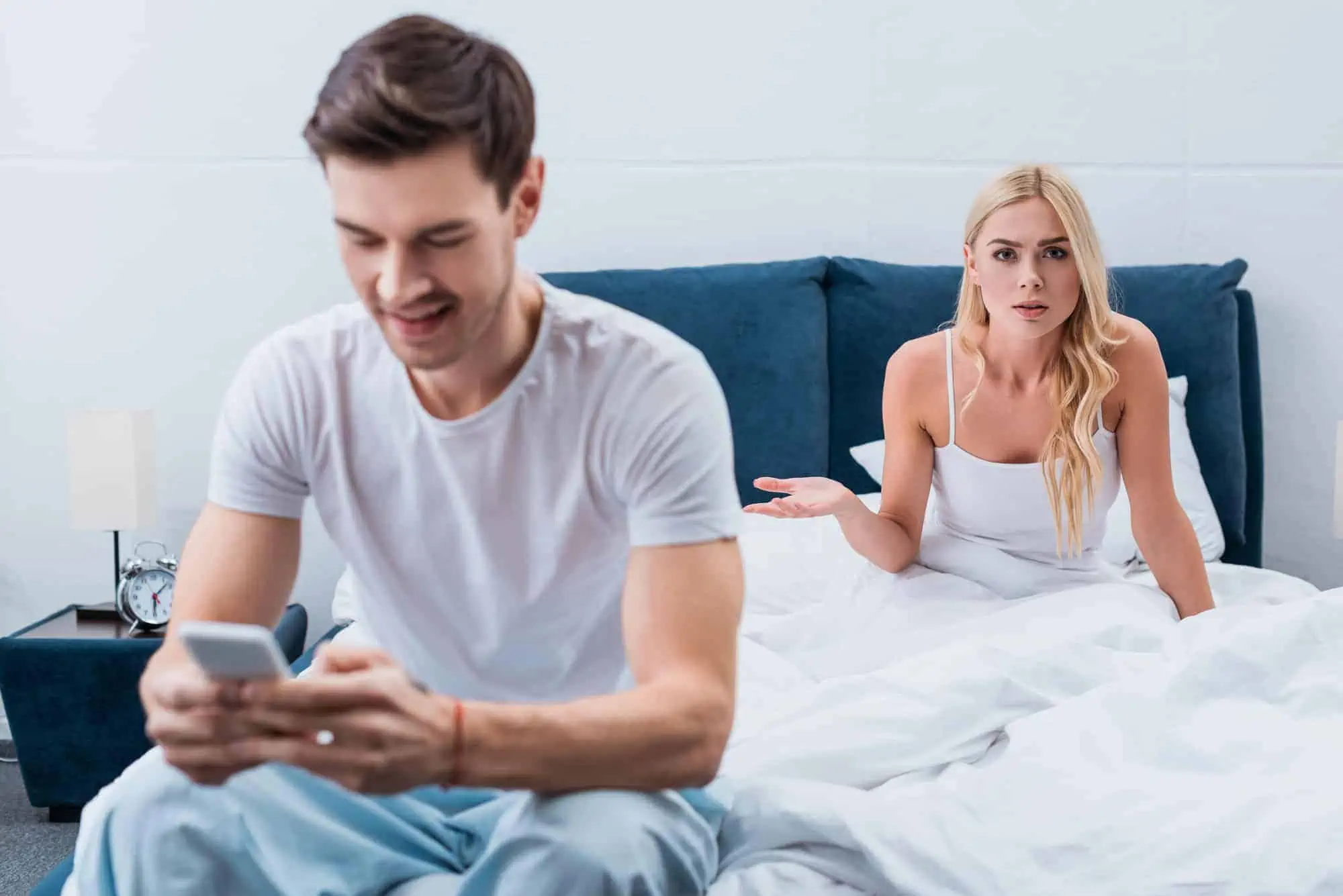 A man and woman sitting on a bed looking at a cell phone