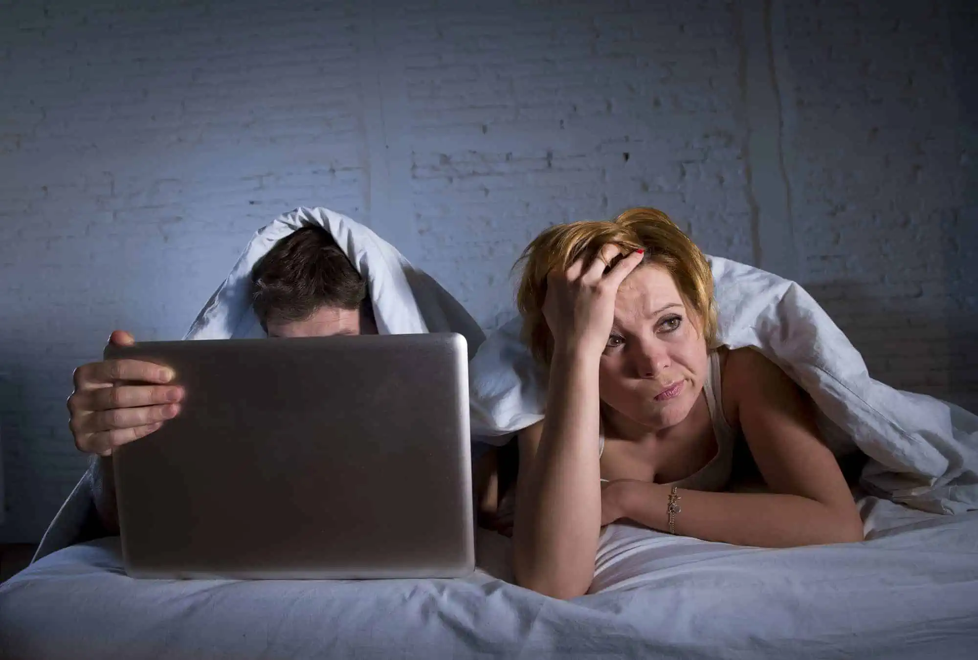 A man and woman laying in bed with a laptop