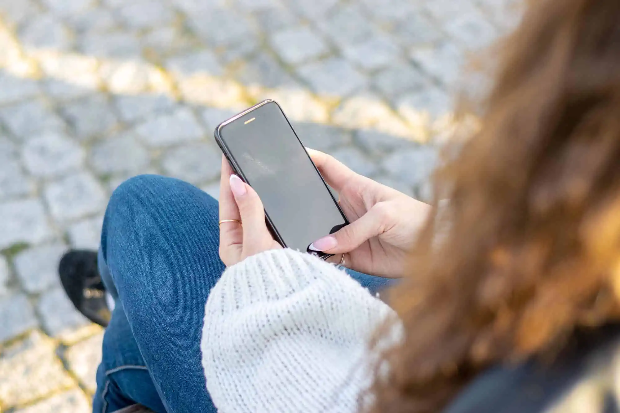 A woman sitting on the ground looking at her cell phone