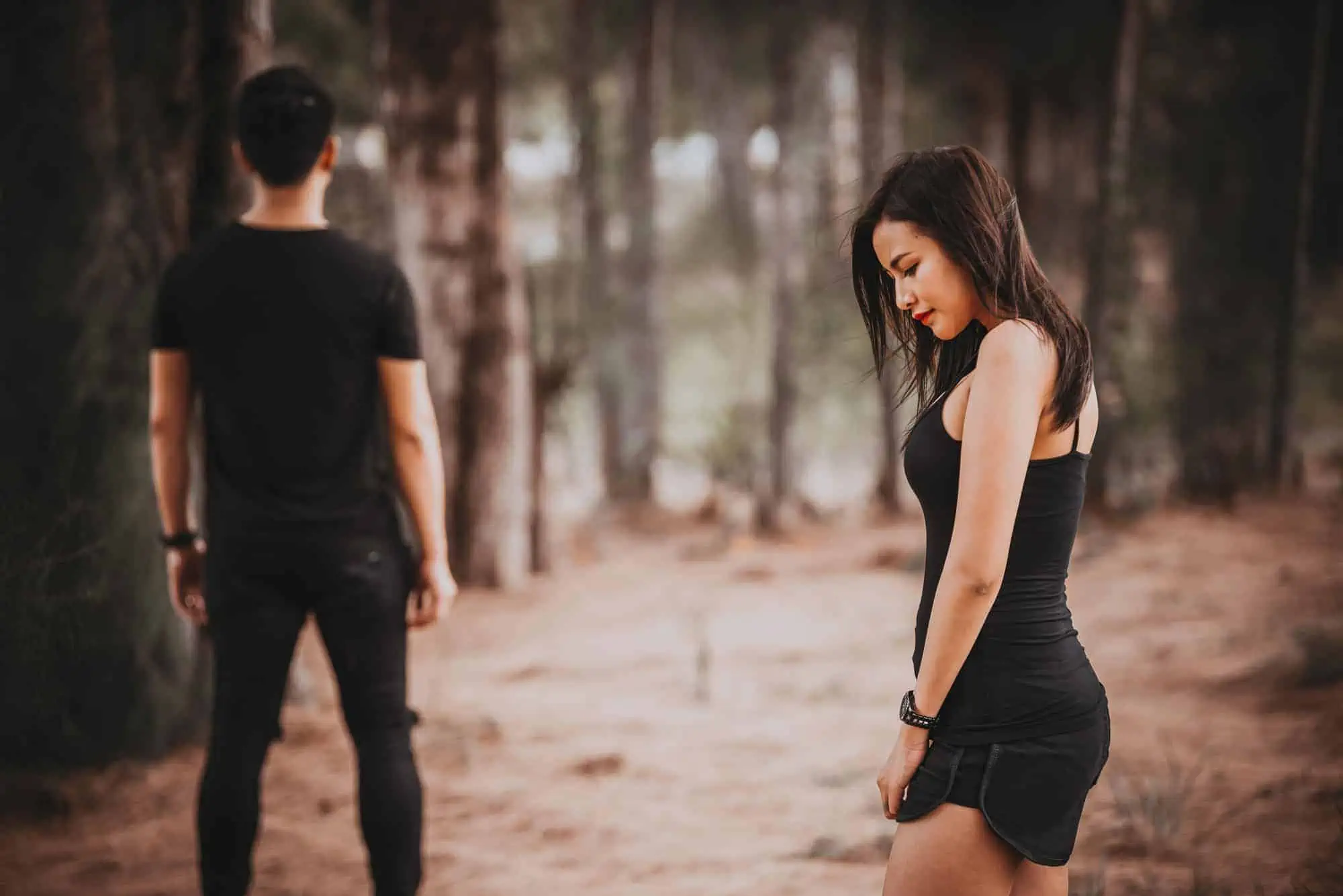 A woman in a black dress standing next to a man in a forest
