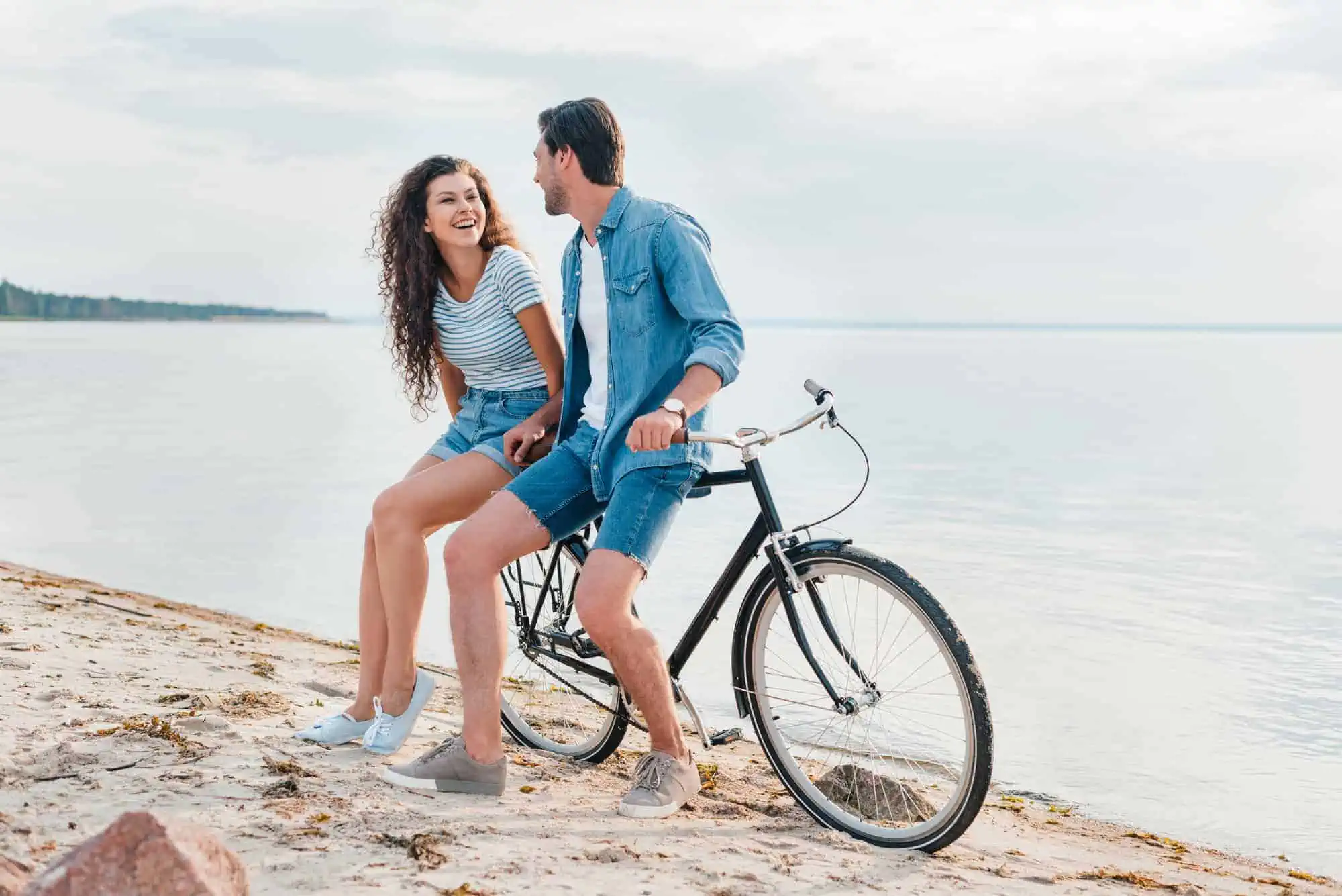 A man and a woman riding a bike on the beach