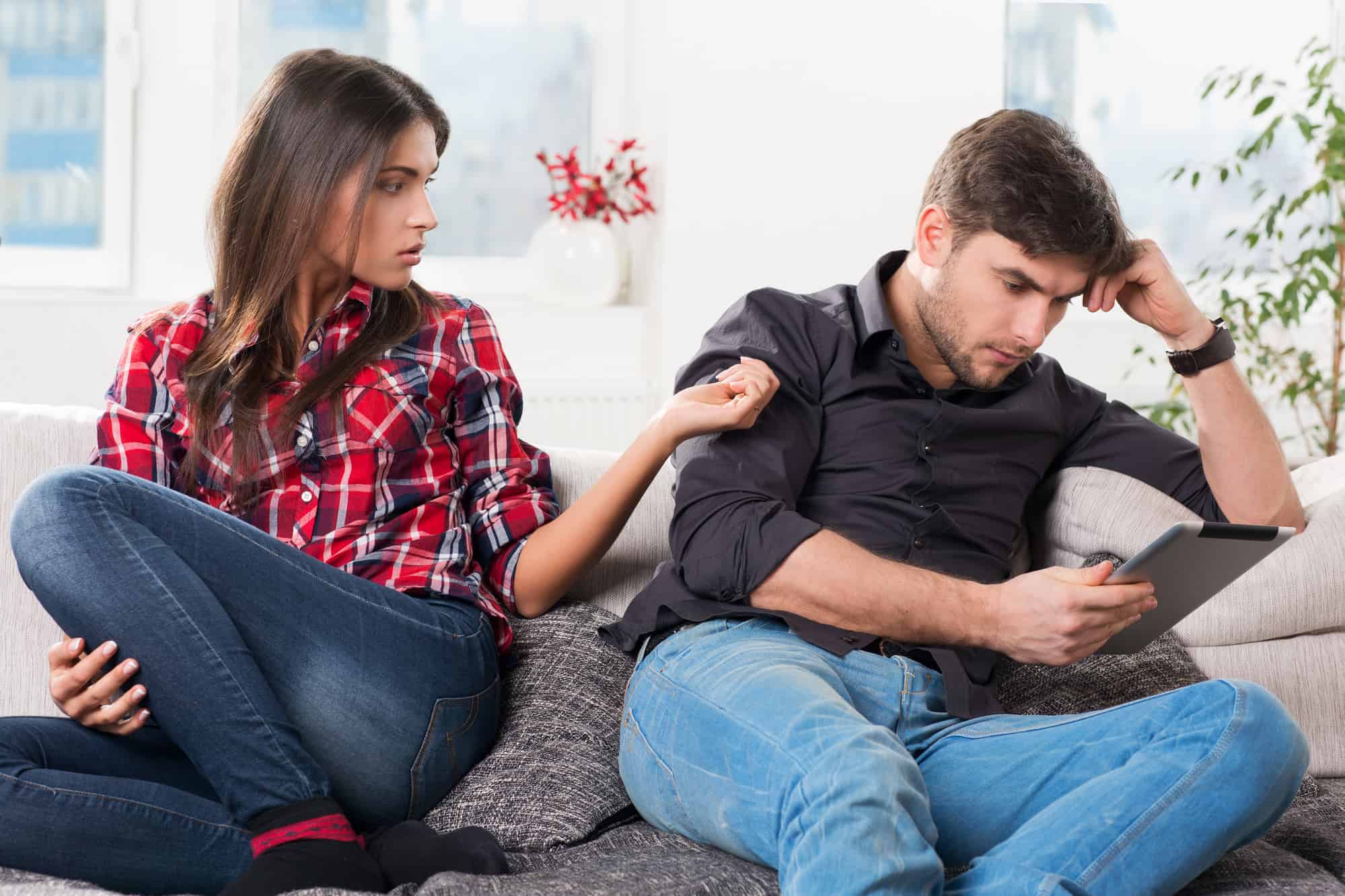 A man and woman sitting on a couch looking at a tablet