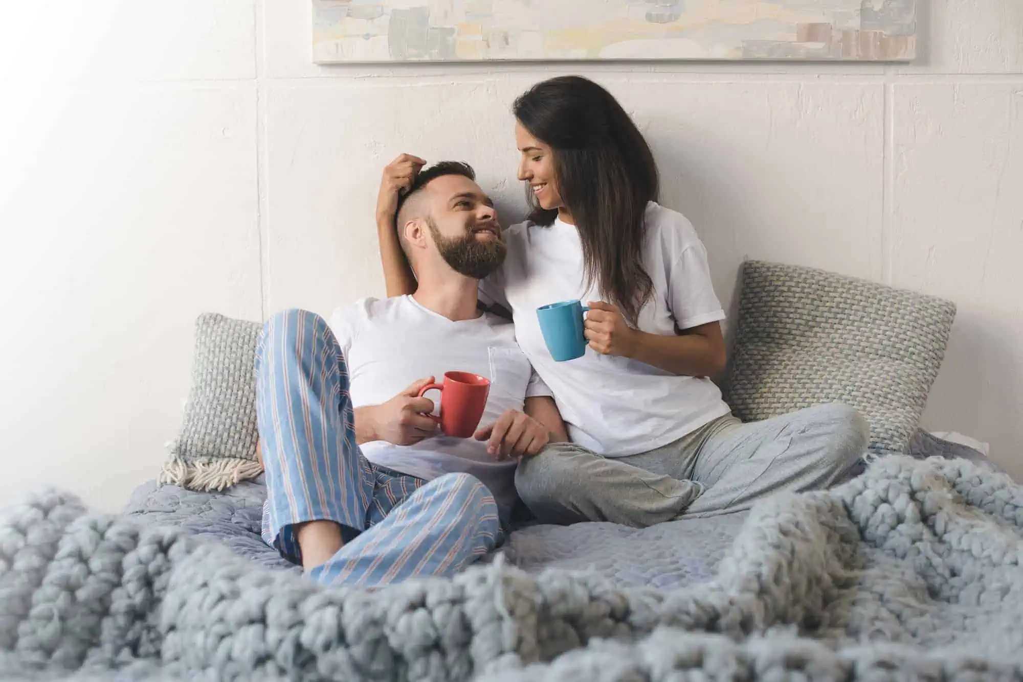 A man and woman sitting on a bed with a cup of coffee